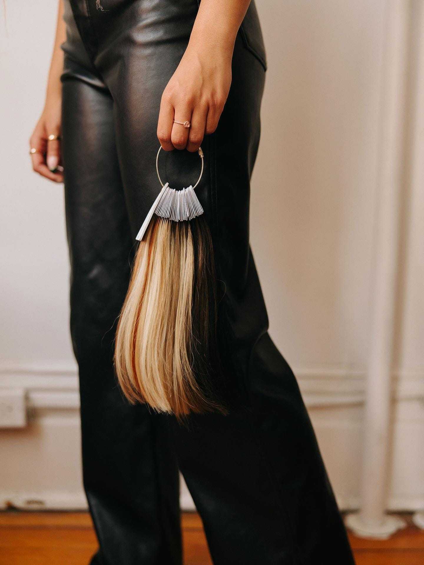 Woman holding hair color samples, wearing black leather pants.