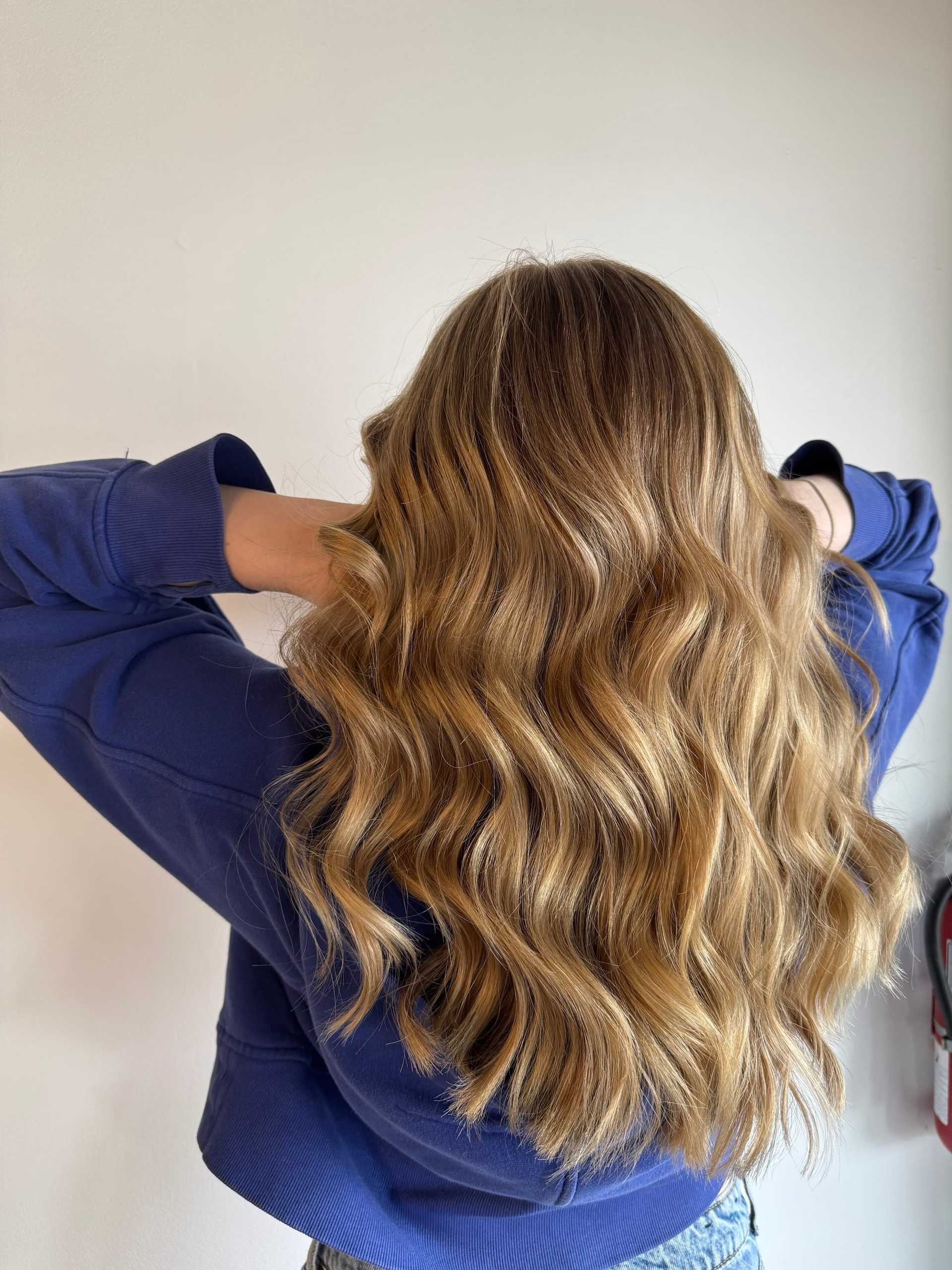 Woman with long, wavy blond hair in a blue sweater, facing away.