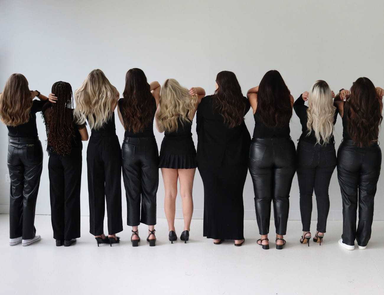 Group of nine women standing in a row, facing away, showing diverse hairstyles and outfits.