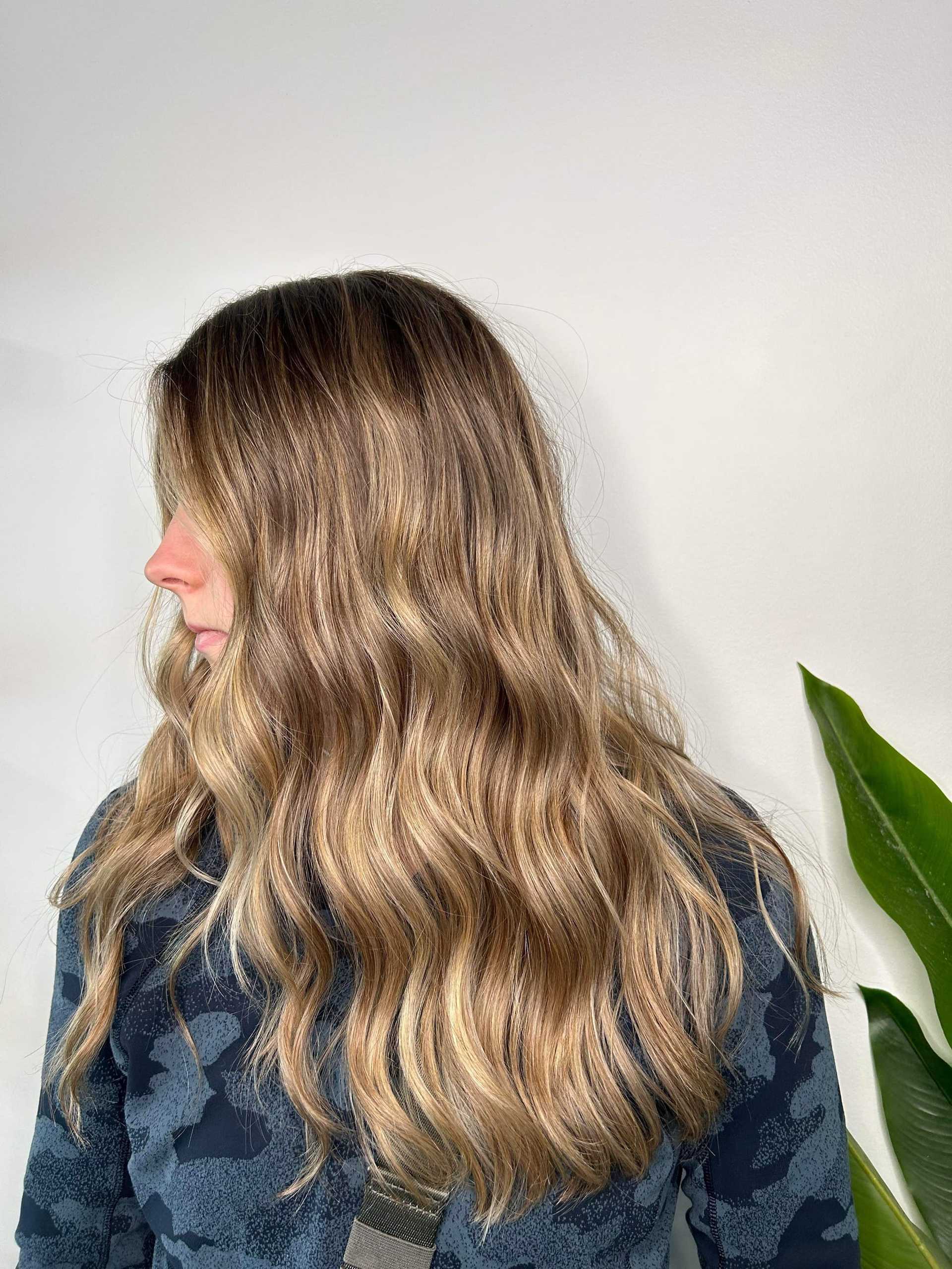 Wavy blonde hairstyle on a woman with a leafy plant background.