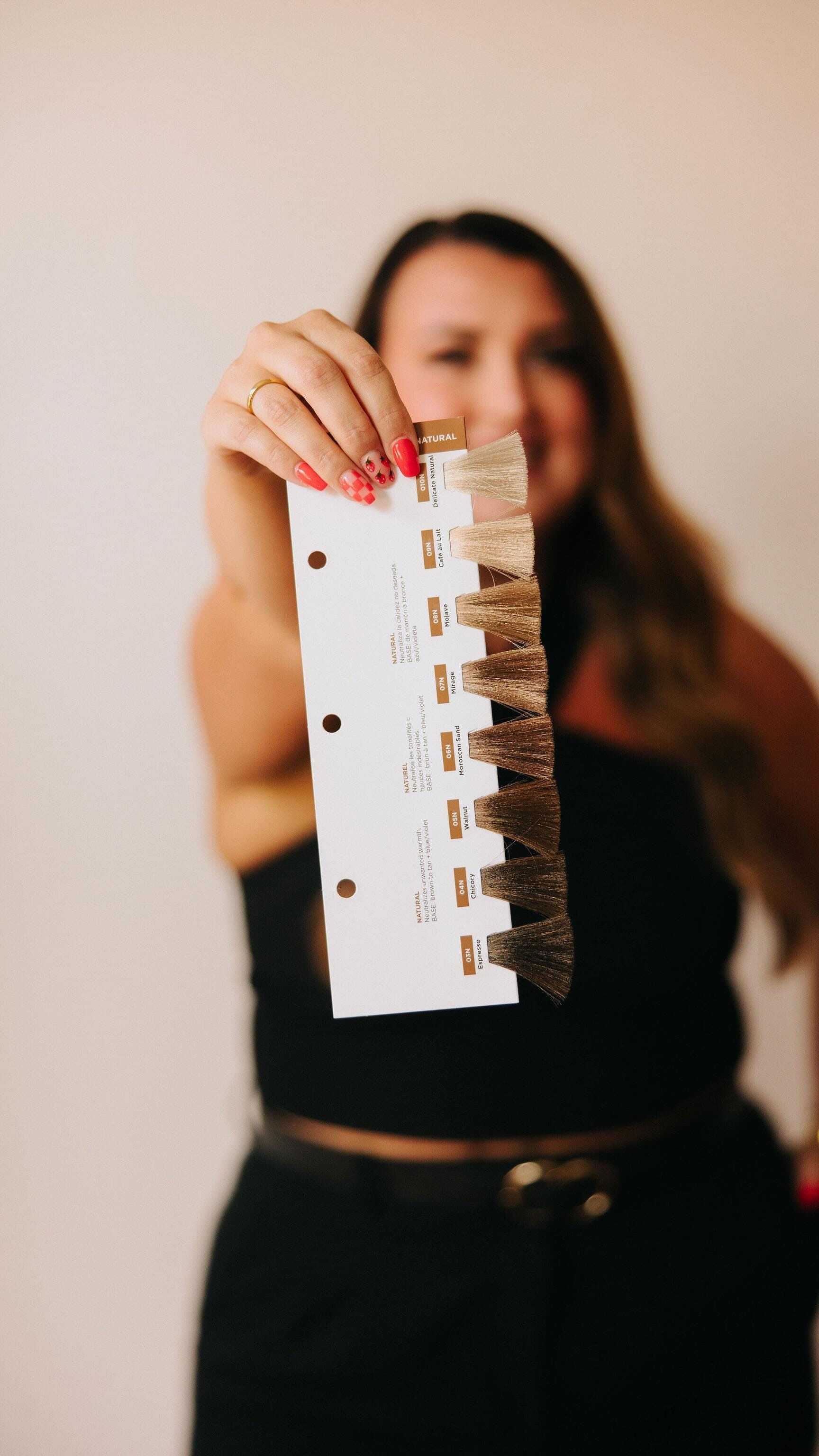 A person holding a hair color sample card with various shades and labels.