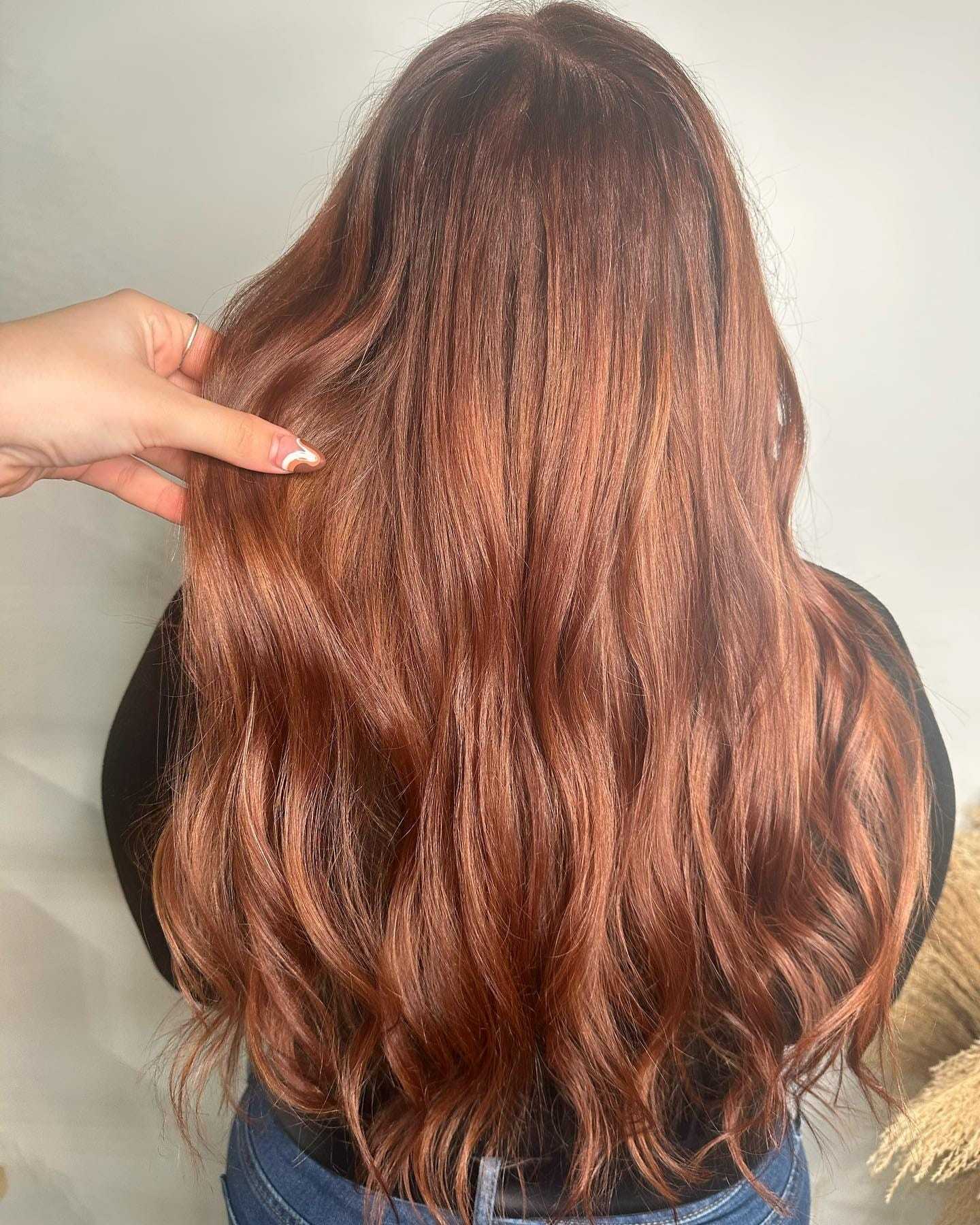 Long wavy auburn hair with highlighted strands, styled and held by a hand.
