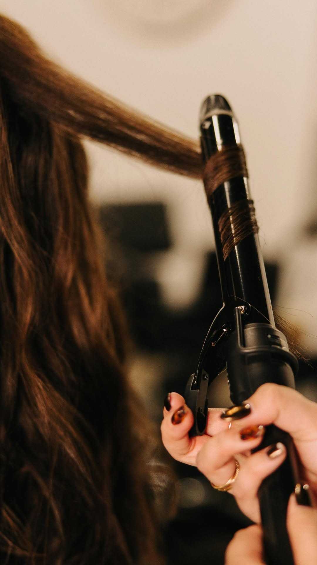 Curling iron styling brunette hair in a salon setting.