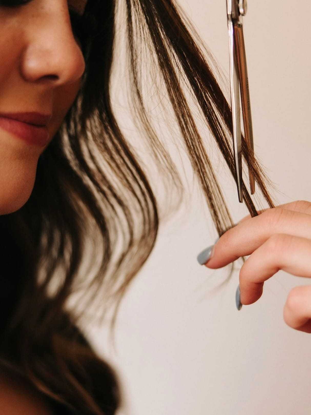 Close-up of a woman cutting her hair with silver scissors.