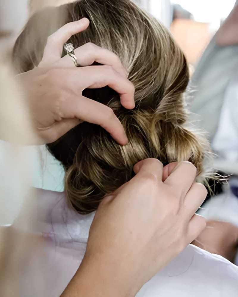 Hands styling a woman's hair into a bun, focusing on the detailed work on the updo.