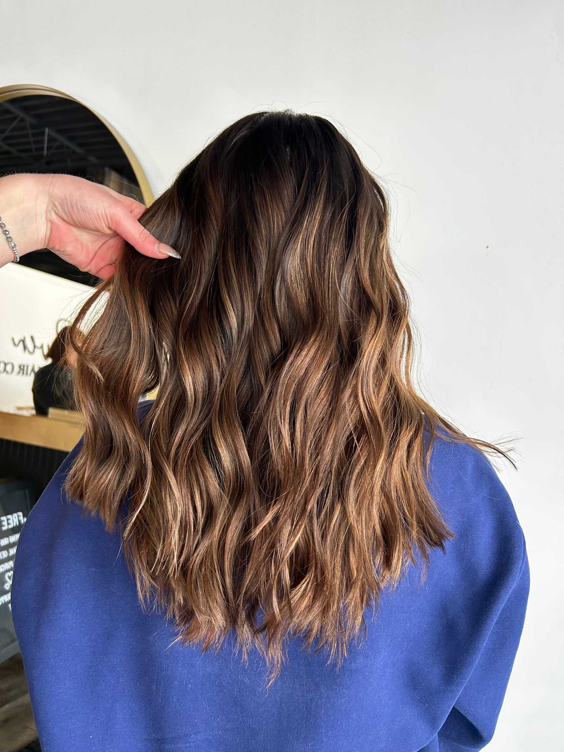 Wavy brunette hair with soft highlights, styled in layers, viewed from the back.