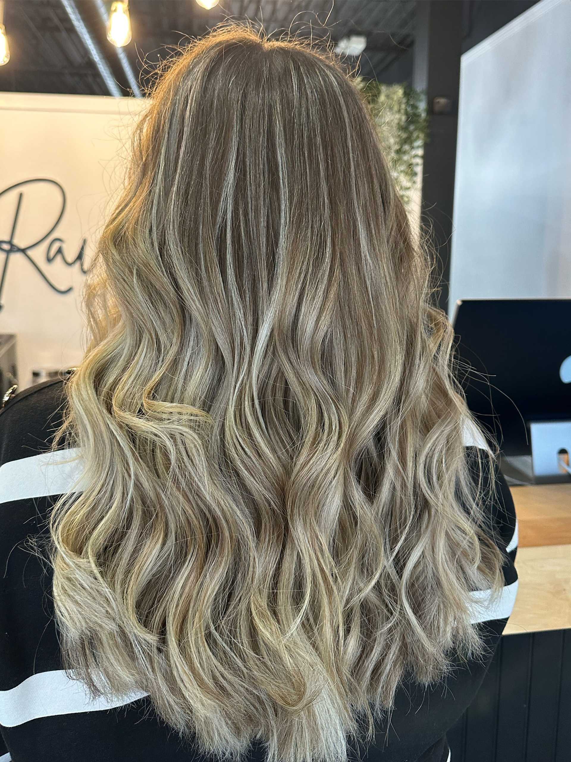 Long wavy blonde hair styled in a salon with a striped shirt.