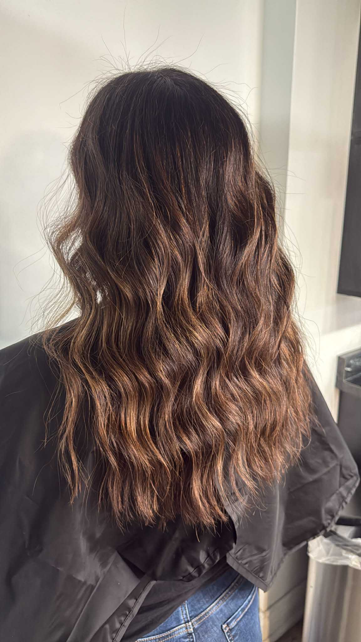 Wavy brunette hair with subtle highlights, styled for volume and texture.